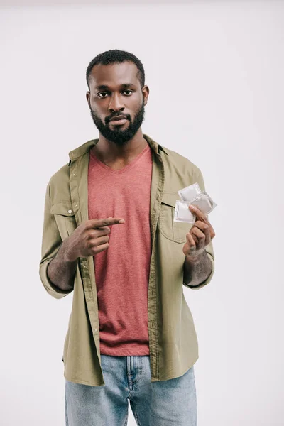Hombre afroamericano guapo serio apuntando a condones aislados en blanco - foto de stock