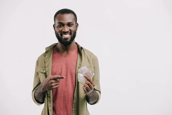 Smiling handsome african american man pointing on condoms isolated on white — Stock Photo