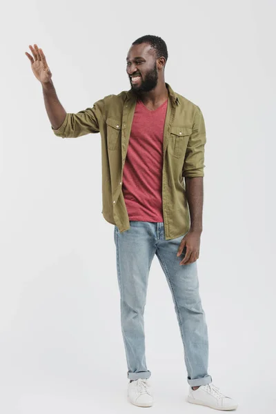 Sonriente guapo afroamericano hombre saludando de la mano y mirando hacia otro lado aislado en blanco - foto de stock