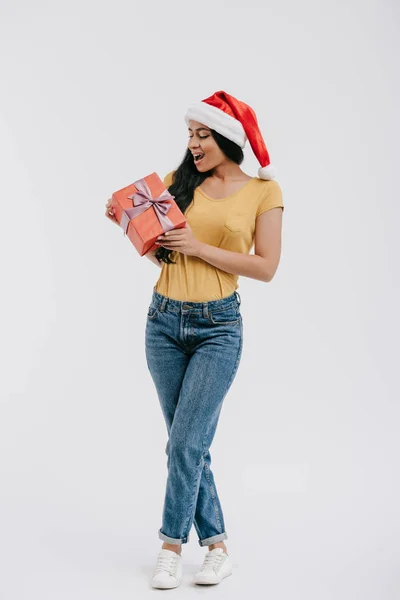 Excited attractive african american girl in santa hat holding present isolated on white — Stock Photo