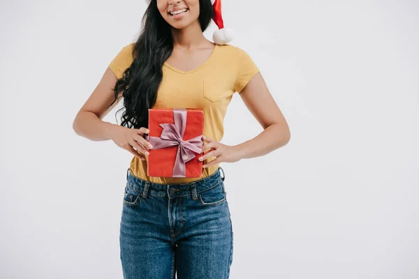 Abgeschnittenes Bild eines lächelnden afrikanisch-amerikanischen Mädchens mit Weihnachtsmannmütze, das Geschenk isoliert auf Weiß hält — Stockfoto