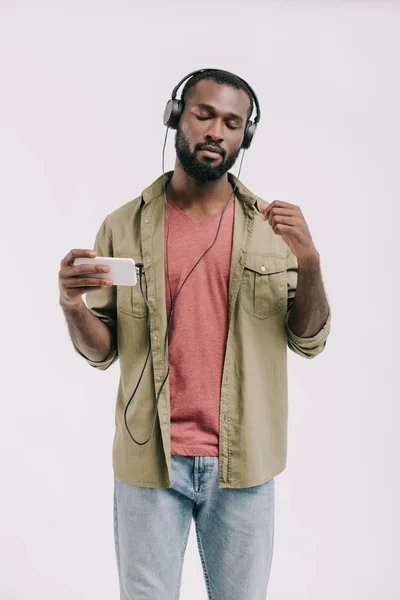 Hombre afroamericano guapo escuchando música con teléfono inteligente y auriculares aislados en blanco - foto de stock