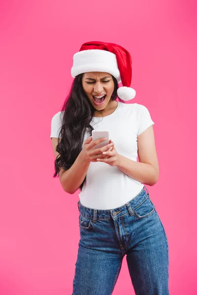 African american girl in santa hat screaming and looking at smartphone isolated on pink — Stock Photo