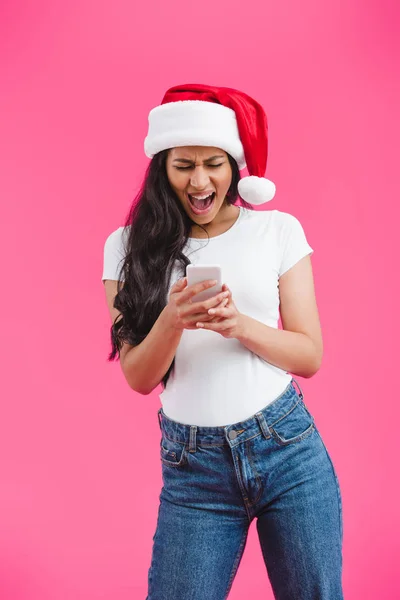 Afrikanisch-amerikanisches Mädchen mit Weihnachtsmütze schreit und schaut auf Smartphone isoliert auf rosa — Stockfoto