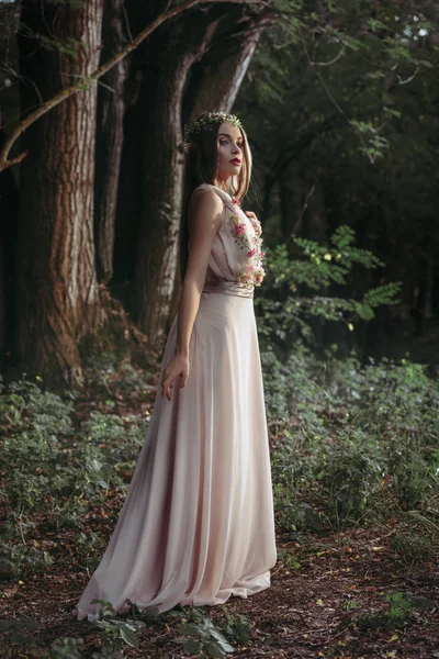 Элегантный мистический эльф в цветочном платье, позирующий в темных лесах — стоковое фото
