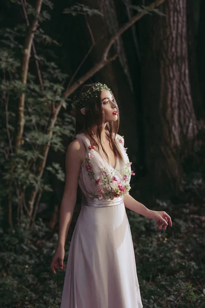Attractive mystic elf in dress with flowers in dark woods — Stock Photo