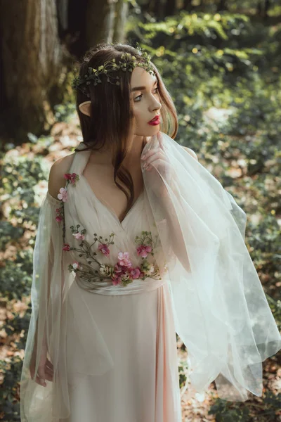 Мистический эльф в элегантном платье с цветами в лесу — стоковое фото