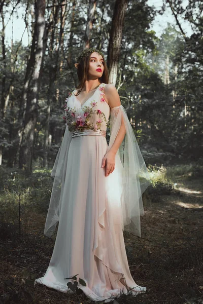 Эльфийский персонаж в цветочном платье и венок, позирующий в лесу — стоковое фото