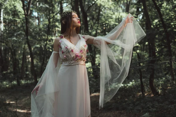 Bellissimo elfo in abito elegante con fiori in posa nella foresta — Foto stock