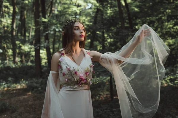 Mystische Elfe in elegantem Kleid mit Blumen im Wald — Stockfoto