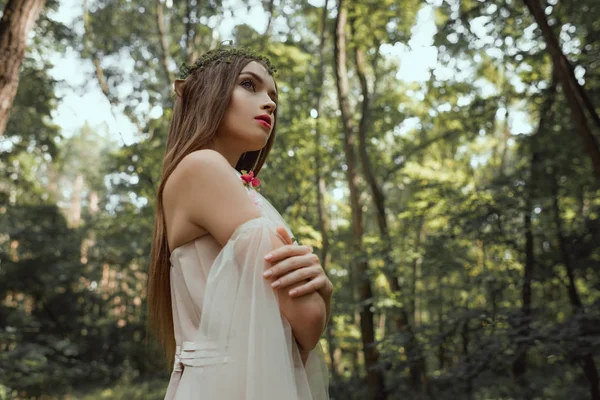 Elegant mystic elf in dress standing with crossed arms in forest — Stock Photo