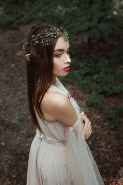 Мистический эльф в элегантном платье и цветочный венок в лесу — стоковое фото