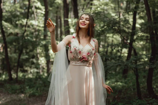 Glückliches Elfenmädchen in elegantem Kleid mit Blumen im Wald — Stockfoto