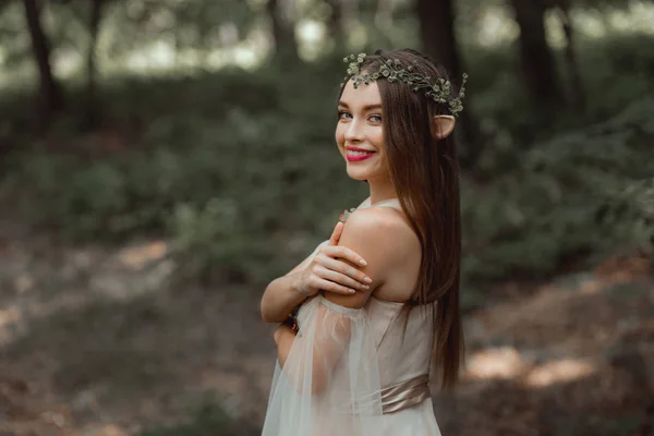 Улыбающаяся девушка с эльфийскими ушами и цветочным венком на голове — стоковое фото