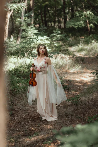 Привабливий містичний ельф в елегантній сукні тримає скрипку в красивому лісі — стокове фото