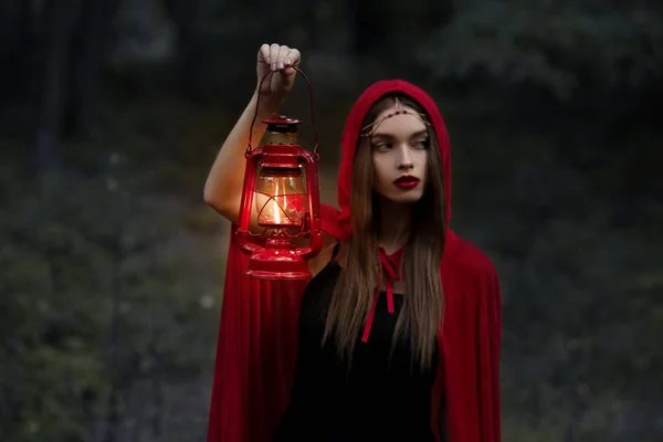Elegant mystic girl walking in dark forest with kerosene lamp — Stock Photo