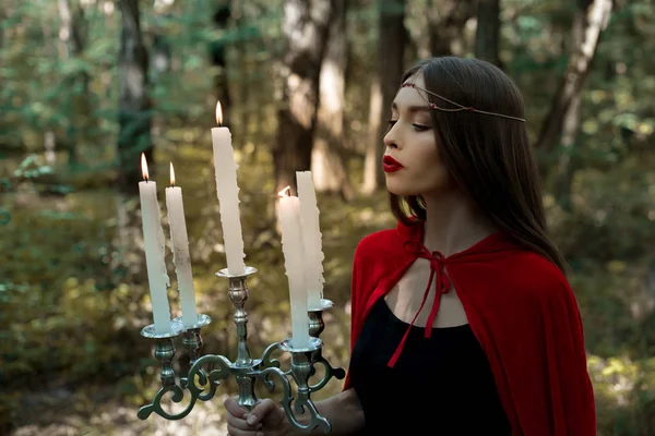 Menina mística atraente segurando candelabro com velas flamejantes na floresta — Fotografia de Stock