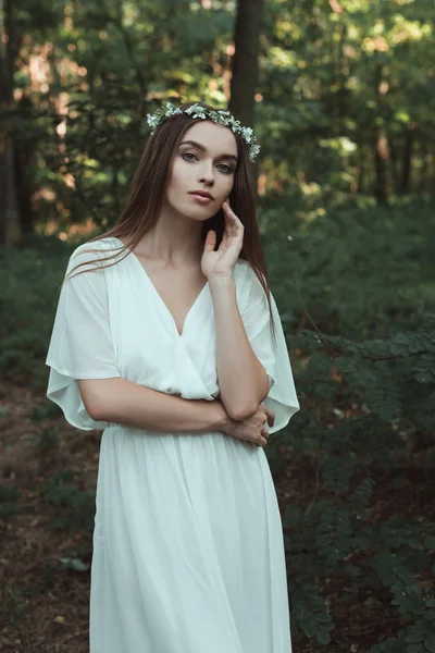 Attraente giovane donna in posa in abito elegante e corona floreale nella foresta — Foto stock