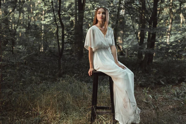 Красива дівчина в білій сукні сидить на табуреті в лісі — стокове фото