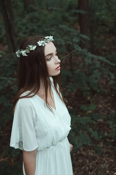 Bela menina macia posando em vestido elegante e coroa floral em madeiras — Fotografia de Stock