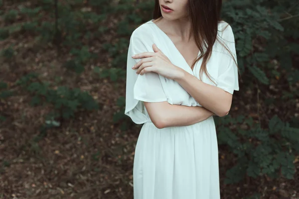 Обрізаний вид ніжної дівчини в білій сукні позує в лісі — стокове фото