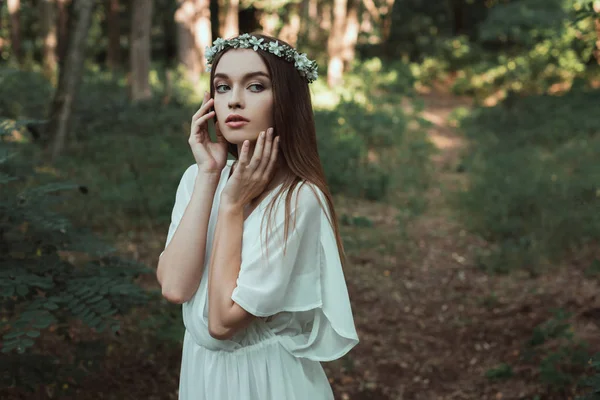 Beautiful tender girl posing in white dress and floral wreath in forest — Stock Photo