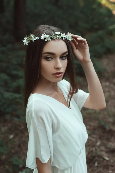 Jovem posando em vestido branco e coroa floral na floresta — Fotografia de Stock