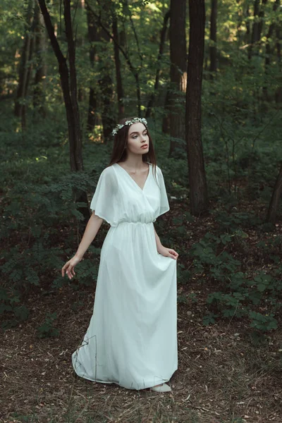 Jolie fille en robe blanche élégante et couronne florale marchant dans les bois — Photo de stock