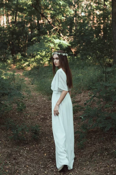 Привлекательная девушка в белом платье и цветочный венок прогулки в лесу — стоковое фото