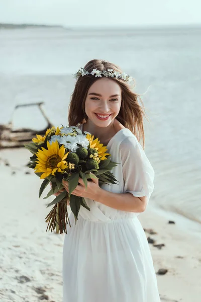 Bela menina feliz em vestido branco segurando girassóis na praia — Fotografia de Stock