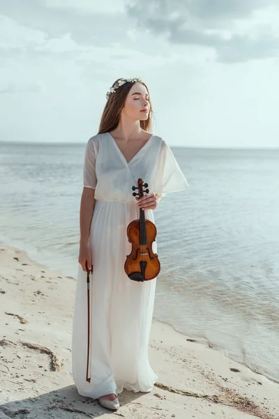 Menina elegante atraente em vestido branco segurando violino na praia — Fotografia de Stock