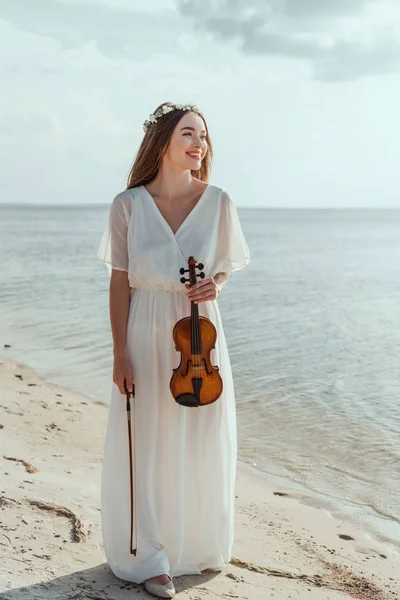 Belle fille souriante en robe élégante tenant violon sur la plage — Photo de stock
