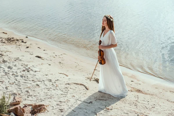 Belle jeune femme en robe élégante tenant violon sur la plage de sable — Photo de stock