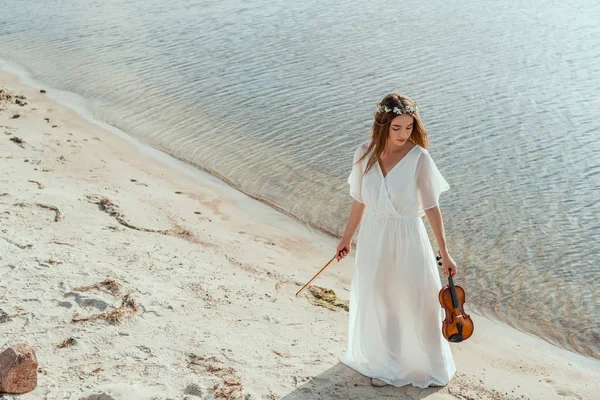 Chica atractiva en vestido blanco sosteniendo violín en la orilla del mar - foto de stock