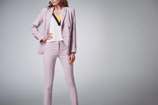 Cropped shot of confident woman in fashionable suit posing with hand on waist isolated on grey — Stock Photo