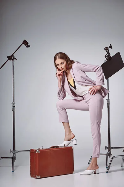 Beautiful fashionable woman posing with suitcase and looking at camera in recording studio — Stock Photo