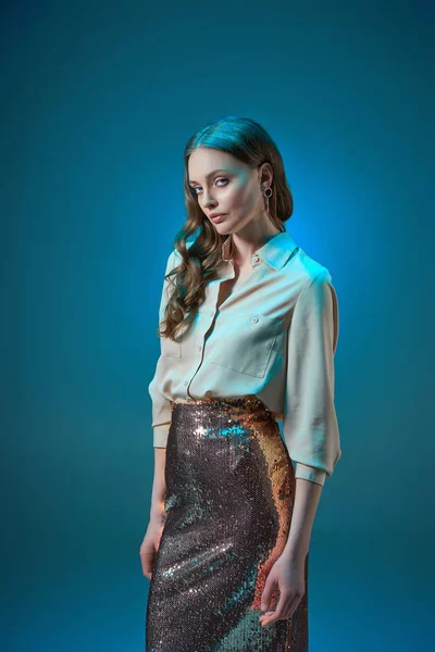 Schöne Frau in modischem goldenem Glitzerrock, die vereinzelt auf blauem Grund in die Kamera blickt — Stockfoto