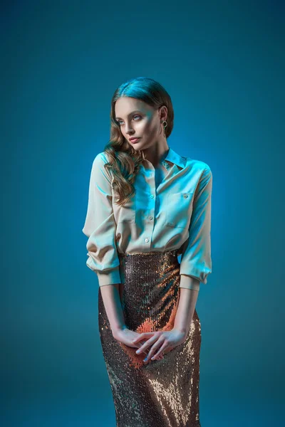 Beautiful woman in fashionable golden glittering skirt looking away isolated on blue — Stock Photo