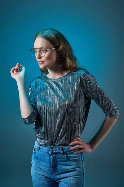 Belle femme élégante dans des lunettes posant avec la main sur la taille et regardant loin isolé sur bleu — Photo de stock