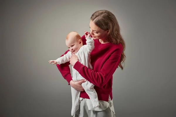 Belle élégante jeune mère souriante et regardant adorable petite fille isolée sur gris — Photo de stock