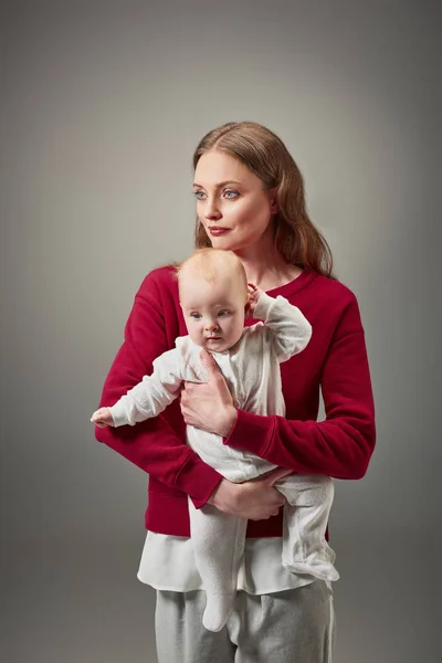 Beautiful stylish mother holding adorable infant daughter isolated on grey — Stock Photo
