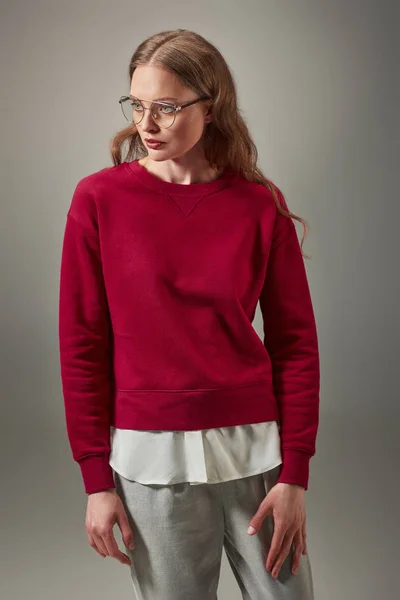 Retrato de mujer hermosa en suéter rojo con estilo y gafas mirando hacia otro lado aislado en gris - foto de stock