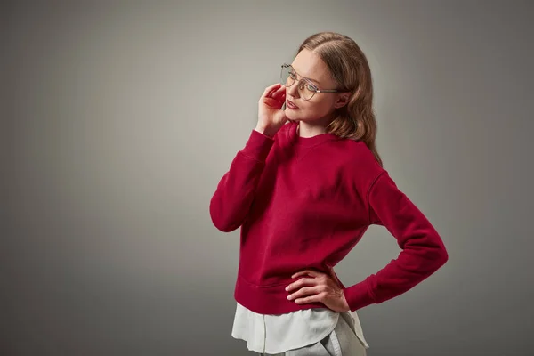 Bella donna in elegante maglione rosso e occhiali guardando lontano isolato sul grigio — Foto stock