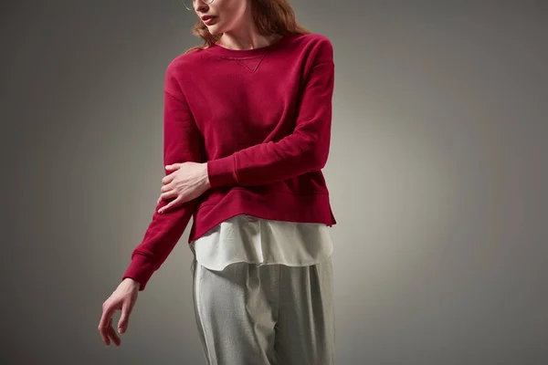 Tiro recortado de mujer en suéter rojo y pantalones elegantes posando aislado en gris - foto de stock