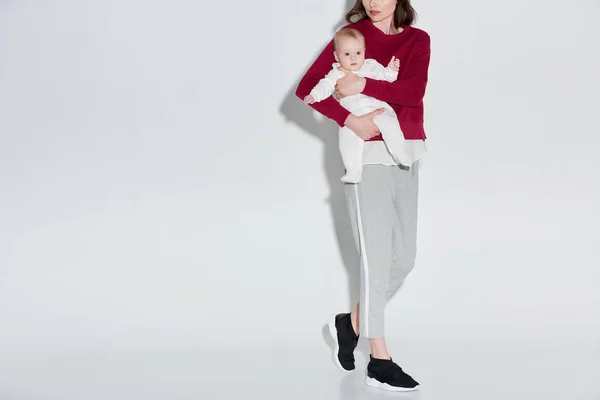 Schnappschuss von stilvoller Mutter, die entzückendes Baby-Mädchen auf grau trägt — Stockfoto