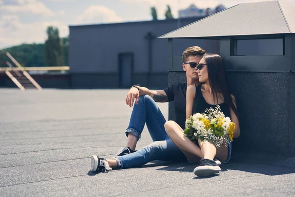Beautiful multicultural couple sitting on asphalt with bouquet of flowers — Stock Photo