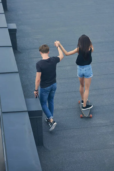 Back view of man holding hands with girlfriend and teaching to ride on skateboard — Stock Photo