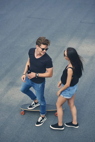 Multicultural couple with bottle of beer on skateboard — Stock Photo
