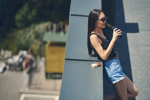 Asian girl drinking beer on roof with cigarette pack — Stock Photo
