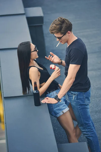 Couple multiethnique chaud avec des cigarettes et une bouteille de bière passer du temps sur le toit — Photo de stock